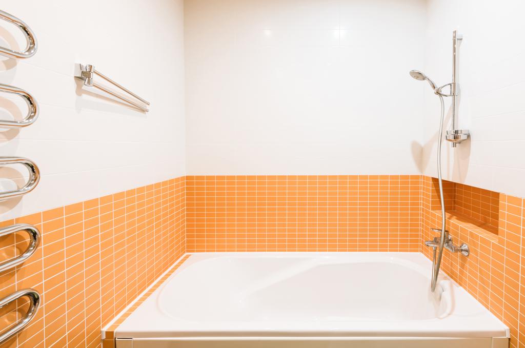vista de cerca del tubo de baño en el baño en colores naranja y blanco
 - Foto, Imagen