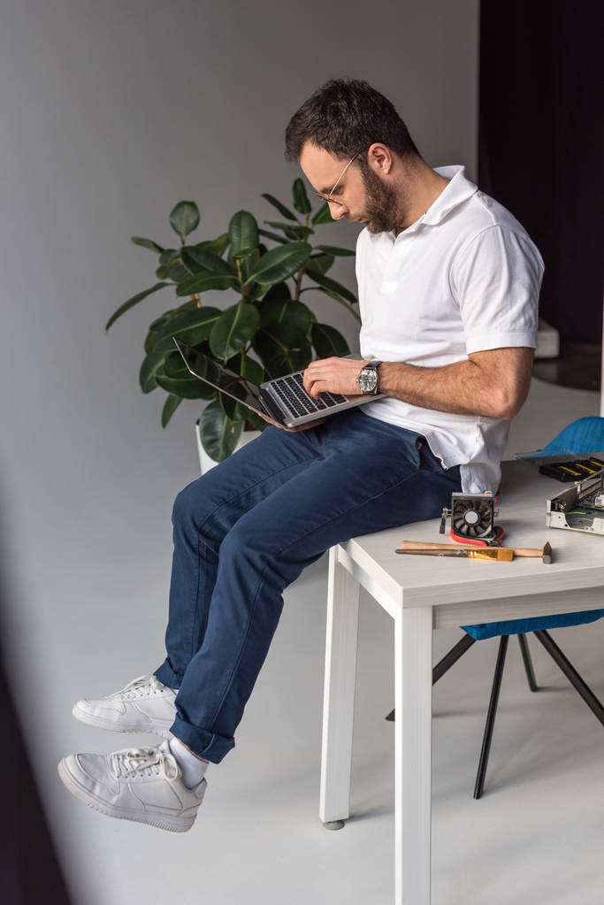 człowiek siedzi na stole i komputera przenośnego  - Zdjęcie, obraz
