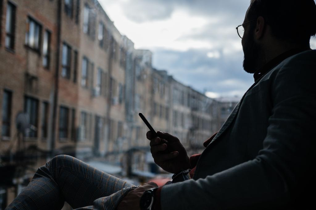 силуэт элегантного мужчины, использующего смартфон и сидящего у окна
 - Фото, изображение