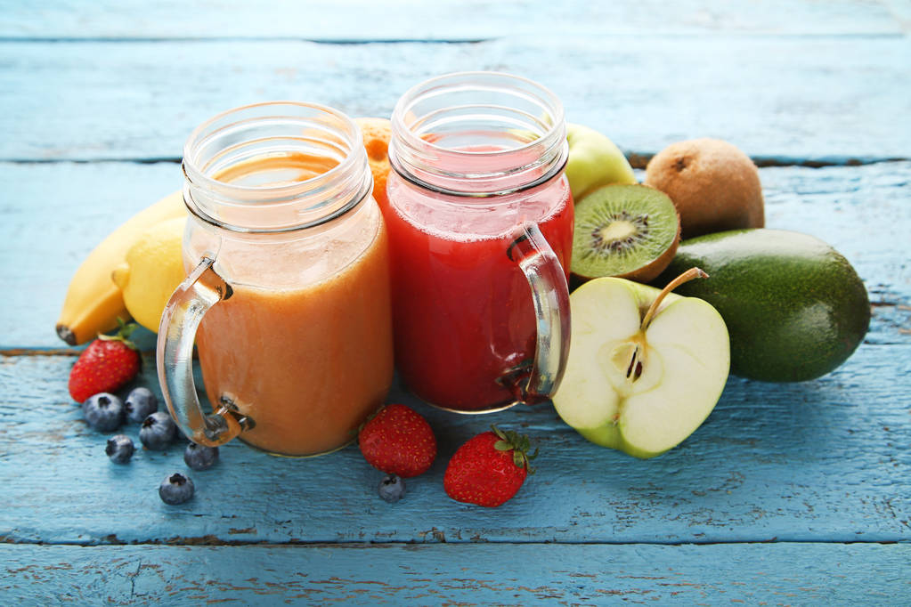 Sweet smoothie in glass jars with fruits on blue wooden table - Photo, Image