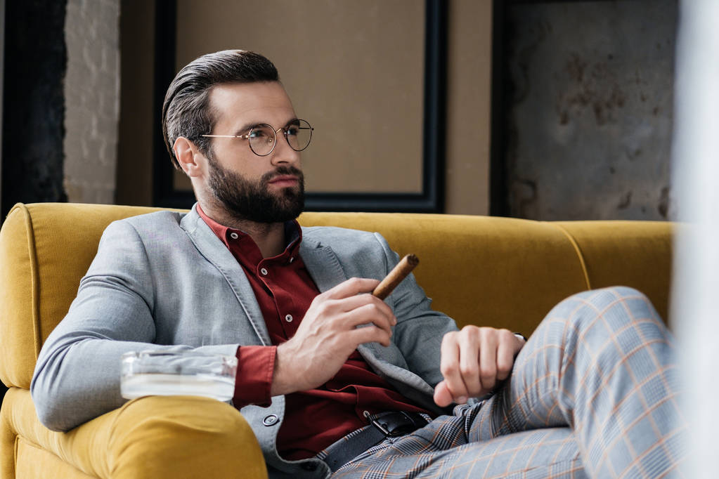 modischer Mann mit Zigarre und Aschenbecher auf Couch sitzend - Foto, Bild