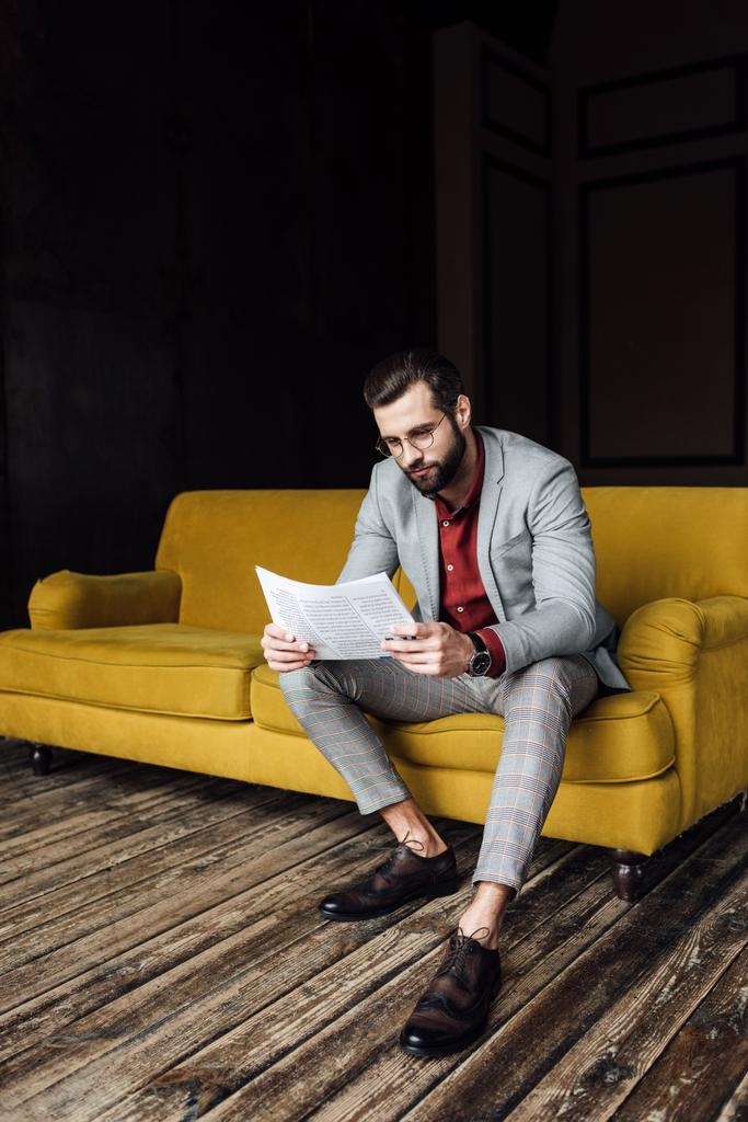 καλαίσθητο άνθρωπος στο κοστούμι διαβάζοντας εφημερίδα και κάθεται στον καναπέ κίτρινο  - Φωτογραφία, εικόνα