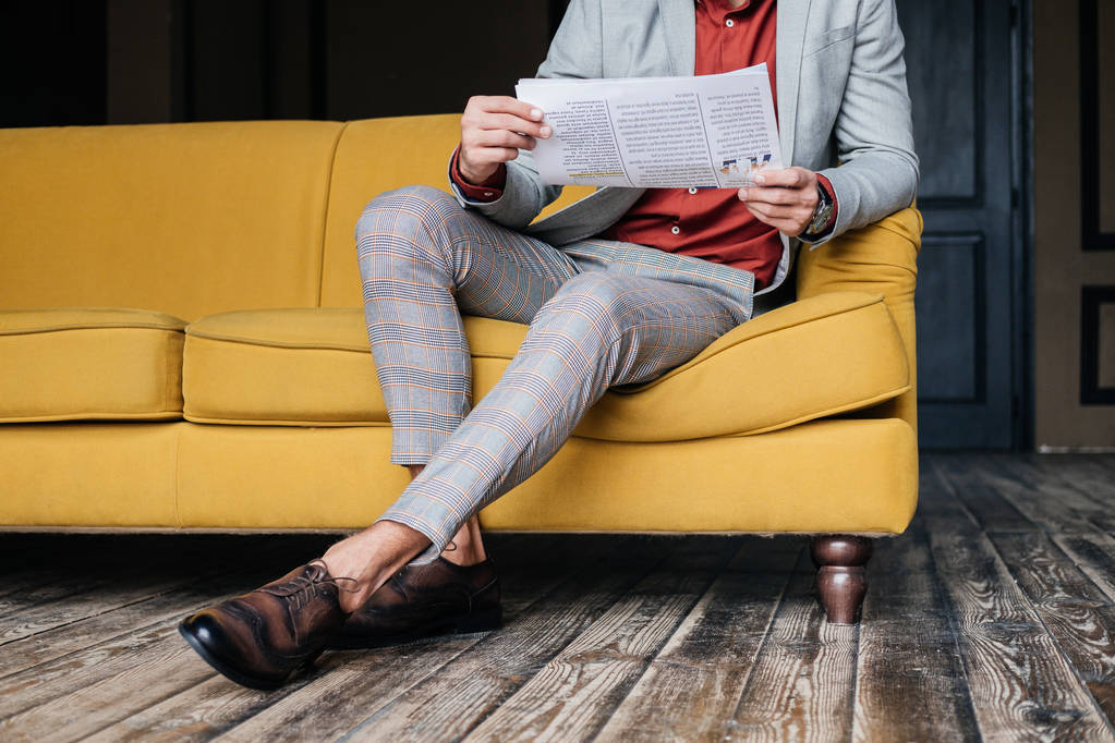 vista ritagliata di uomo elegante seduto sul divano con giornale
 - Foto, immagini