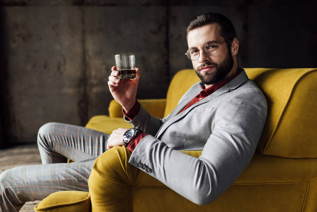 stílusos jóképű férfi, gazdaság pohár whiskyt és látszó-on fényképezőgép - Fotó, kép