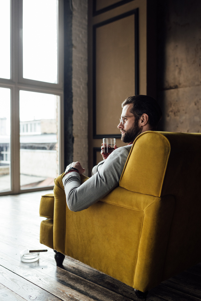 stijlvolle knappe man houden glas whiskey en zittend op de Bank - Foto, afbeelding