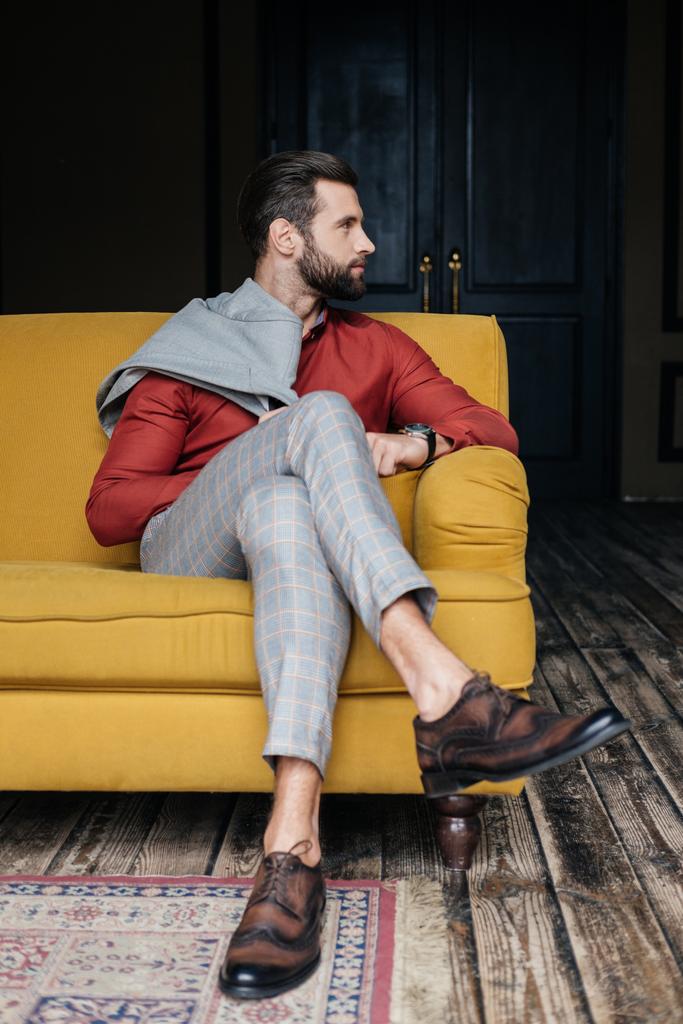modischer Mann in Anzug und Brogue-Schuhen auf gelbem Sofa im Loft-Interieur - Foto, Bild