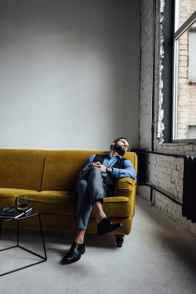 елегантний чоловік відпочиває на жовтому дивані з алкоголем на столі поруч
  - Фото, зображення