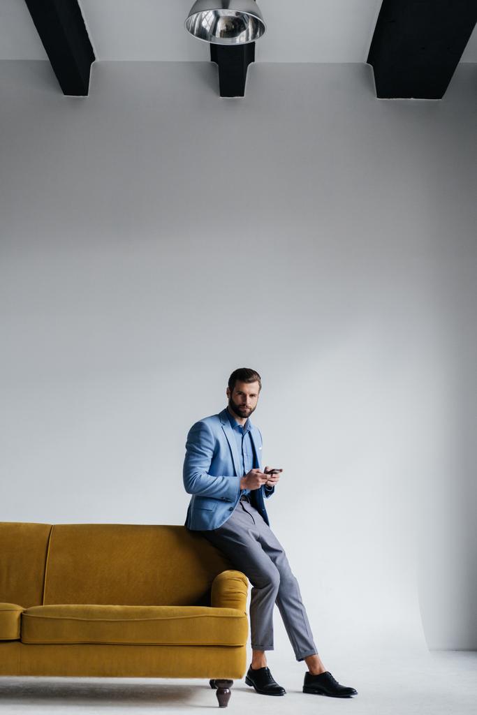 модний чоловік у синьому костюмі використовує смартфон на жовтому дивані
 - Фото, зображення