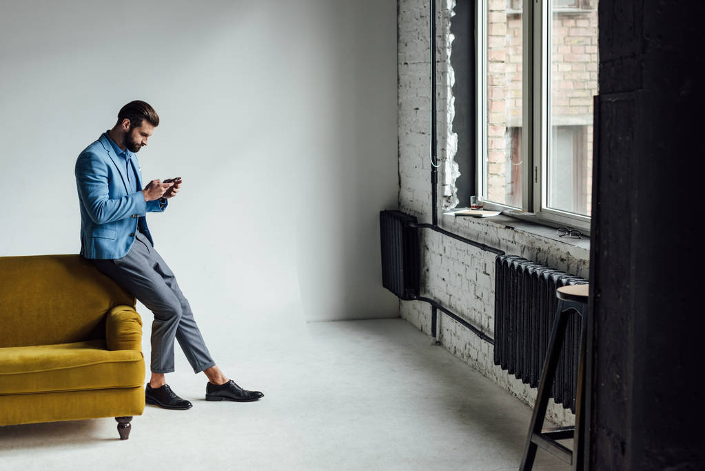 divatos férfi kék színű használ smartphone-on sárga kanapé  - Fotó, kép