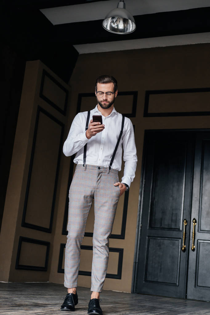 стильный бородатый мужчина в подтяжках, используя смартфон в интерьере лофта
 - Фото, изображение