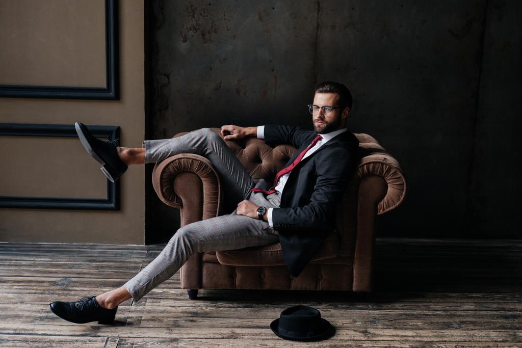 bell'uomo d'affari elegante in posa in poltrona, cappello sdraiato sul pavimento vicino, soppalco interno
 - Foto, immagini
