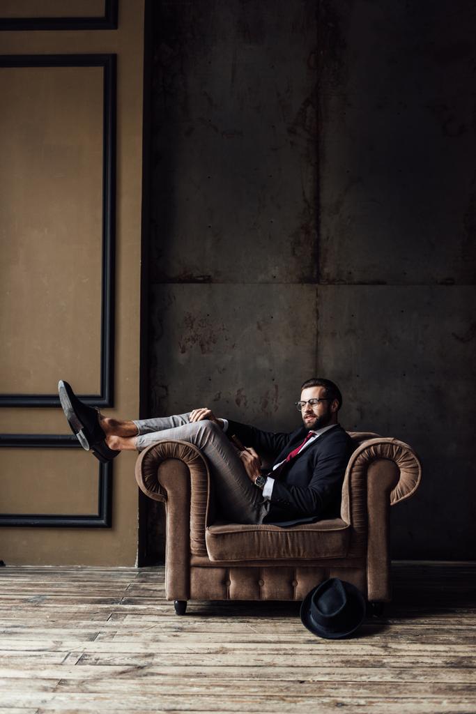 élégant homme d'affaires posant dans un fauteuil, chapeau couché sur le sol près, intérieur loft
  - Photo, image