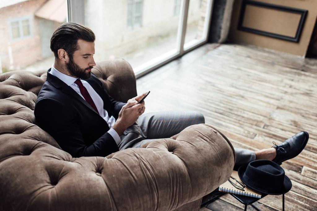 αυτοπεποίθηση κομψό επιχειρηματίας χρησιμοποιώντας smartphone και κάθεται στην πολυθρόνα  - Φωτογραφία, εικόνα