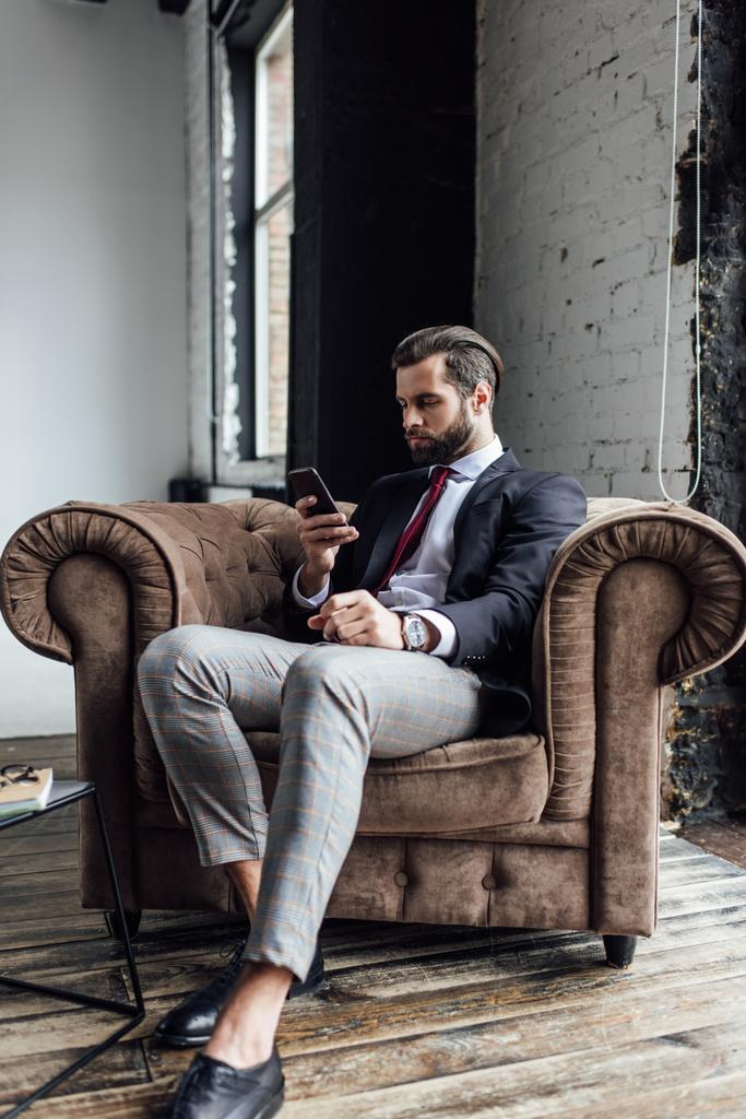 уверенный в себе бизнесмен смс на смартфоне, сидя в кресле на чердаке
 - Фото, изображение