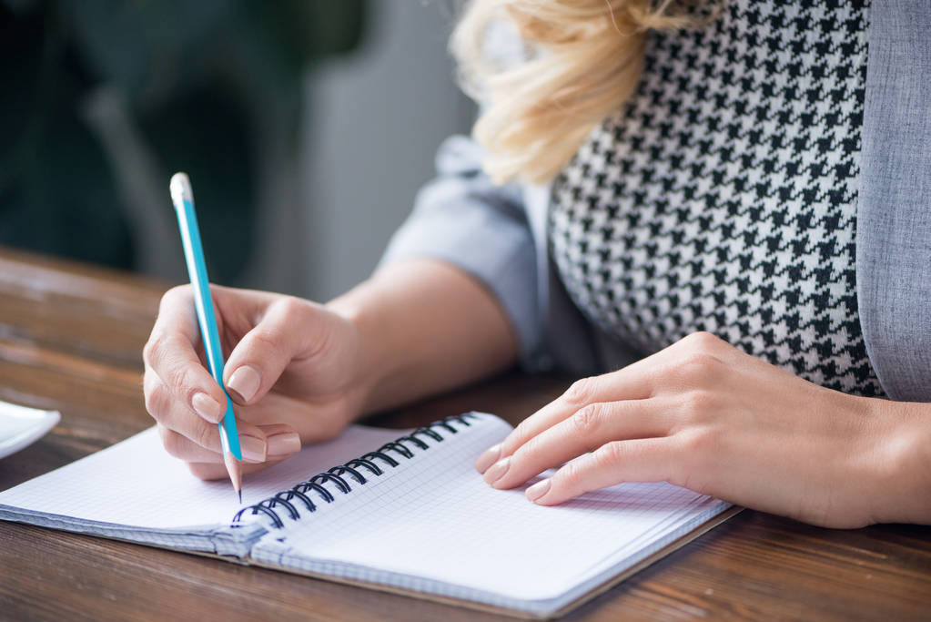 imagen recortada de la mujer de negocios escribiendo algo a cuaderno con lápiz
 - Foto, Imagen