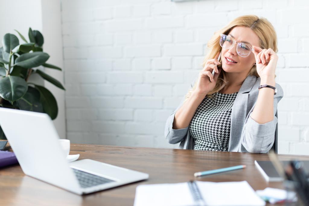 mujer de negocios hablando por teléfono inteligente en la oficina y tocando gafas
 - Foto, Imagen