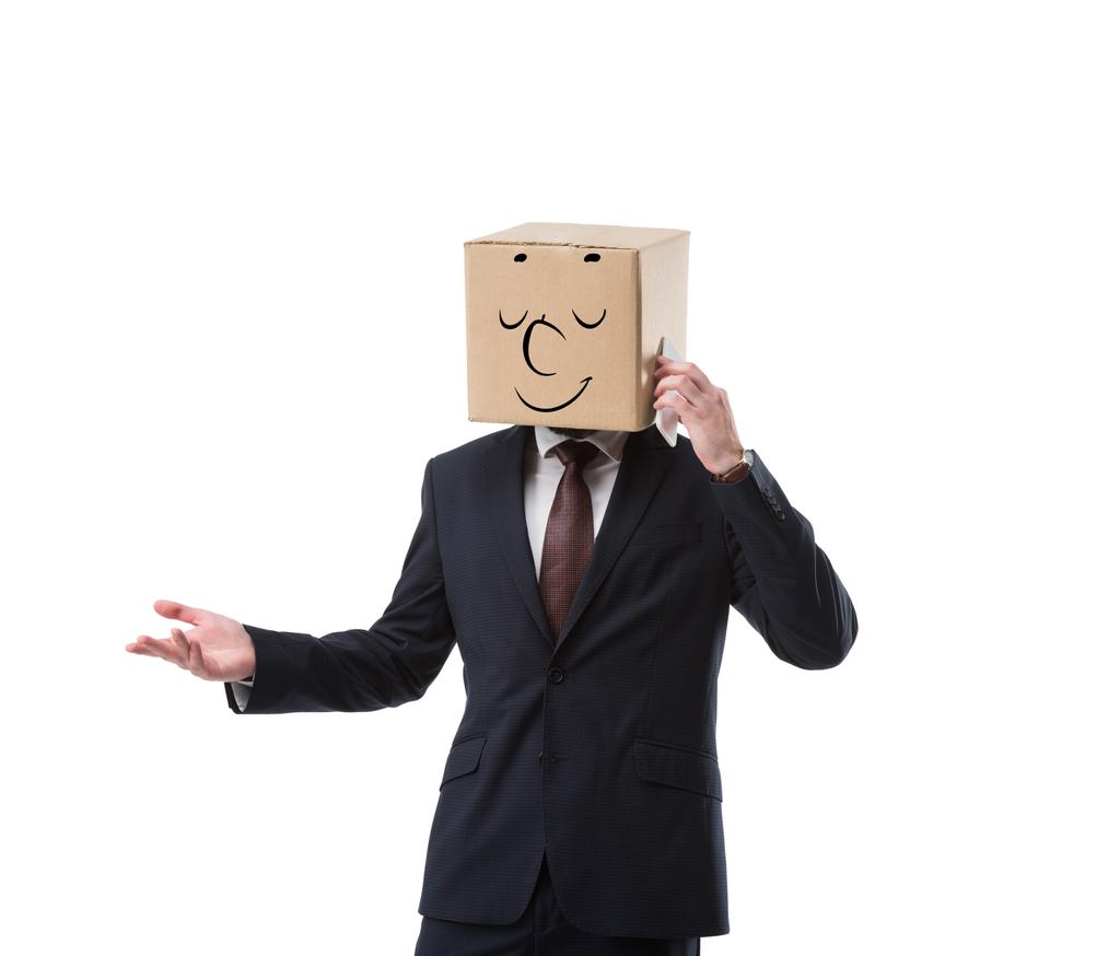 ontspannen zakenman met kartonnen doos op hoofd praten op smartphone geïsoleerd op wit - Foto, afbeelding