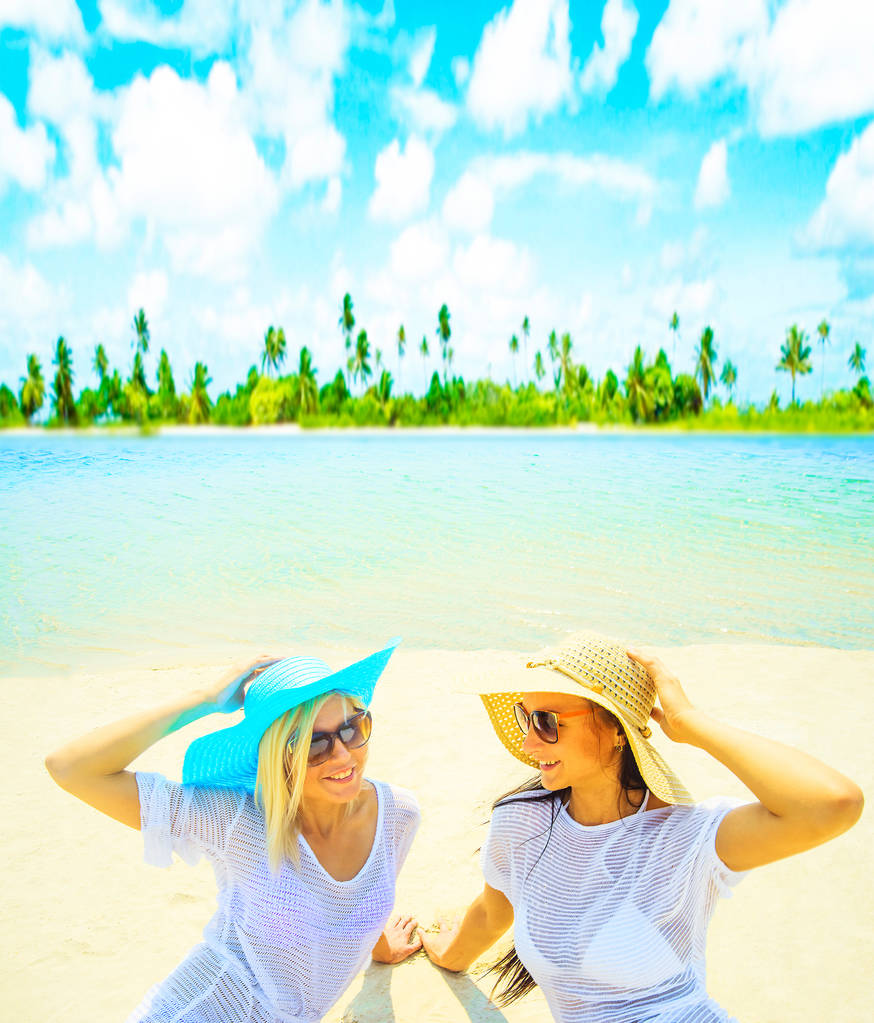 Couple de femmes assises sur du sable blanc chaud contre une plage tropicale
 - Photo, image