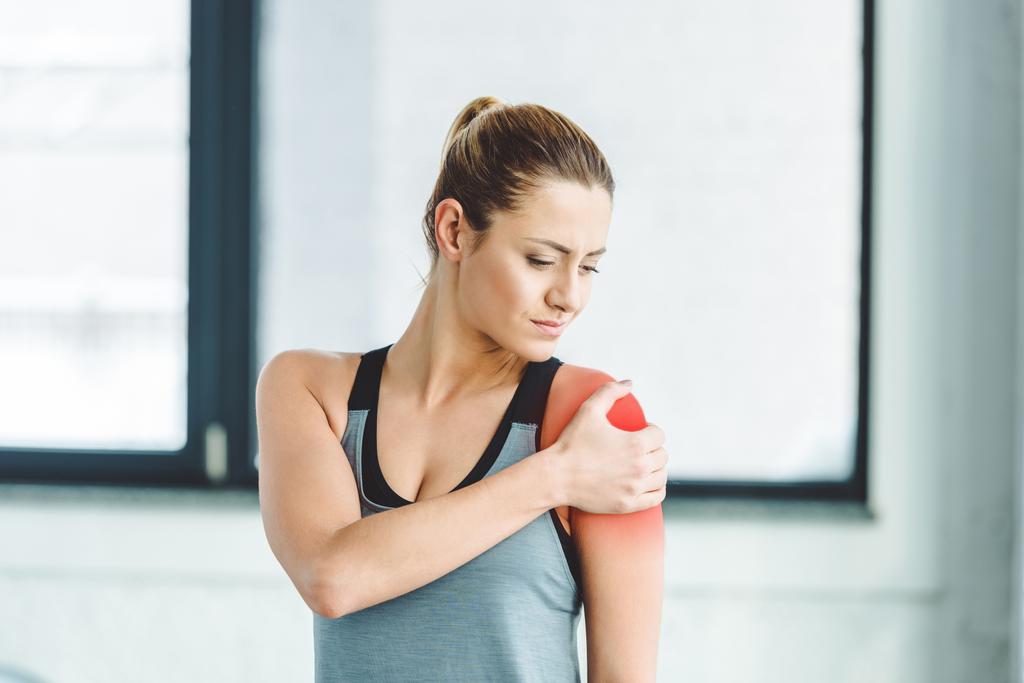 Porträt einer jungen Sportlerin mit Schmerzen im Arm im Fitnessstudio  - Foto, Bild