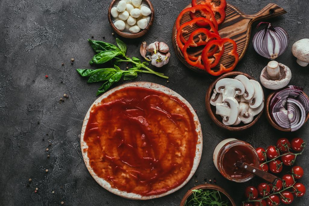 pohled shora surového pizza těsta s omáčkou a zeleninou na betonový stůl - Fotografie, Obrázek