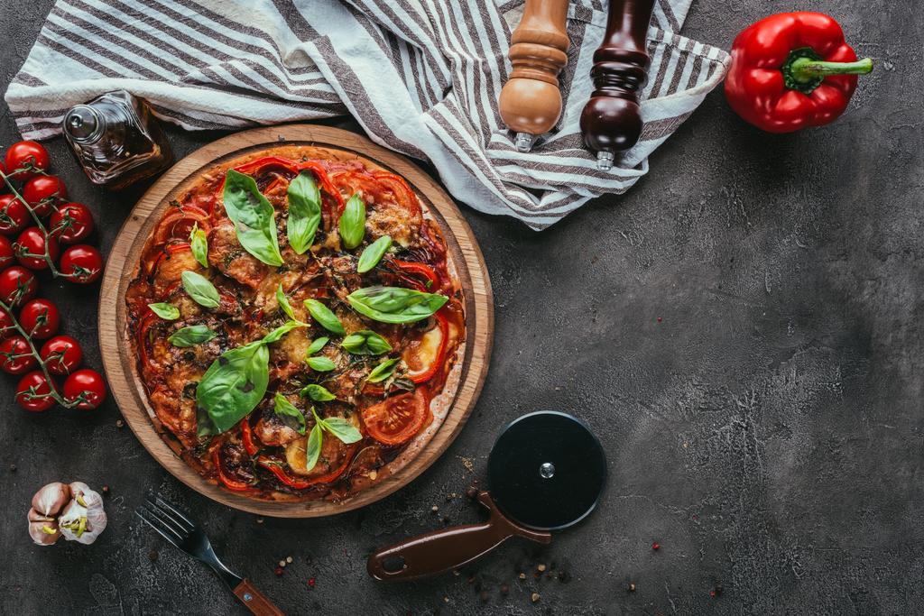 top view of freshly baked pizza with cutter and ingredients on concrete table - Photo, Image
