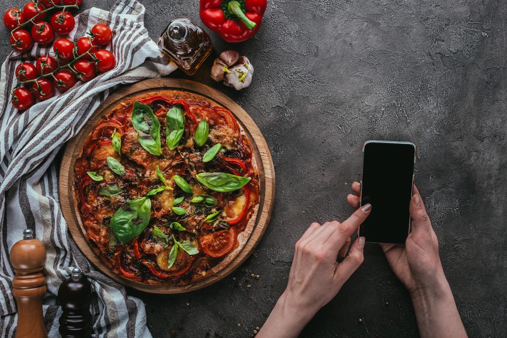 bijgesneden schot van vrouw met behulp van smartphone op betonnen tafel met pizza - Foto, afbeelding
