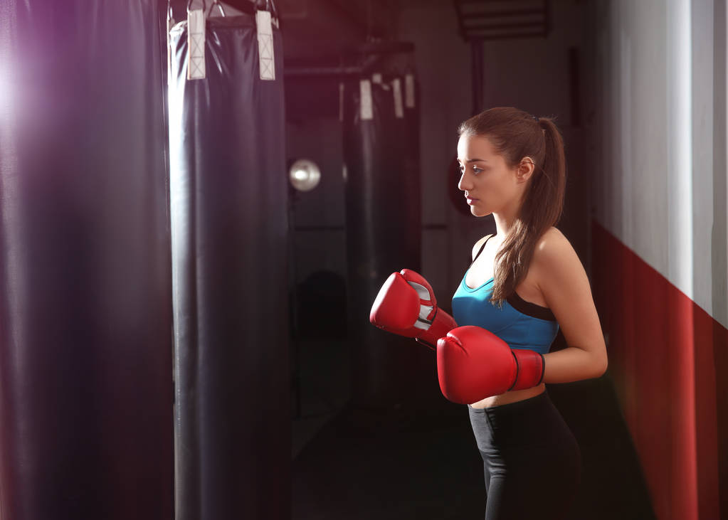 Jonge vrouwelijke bokser die traint met bokszak in sportschool - Foto, afbeelding