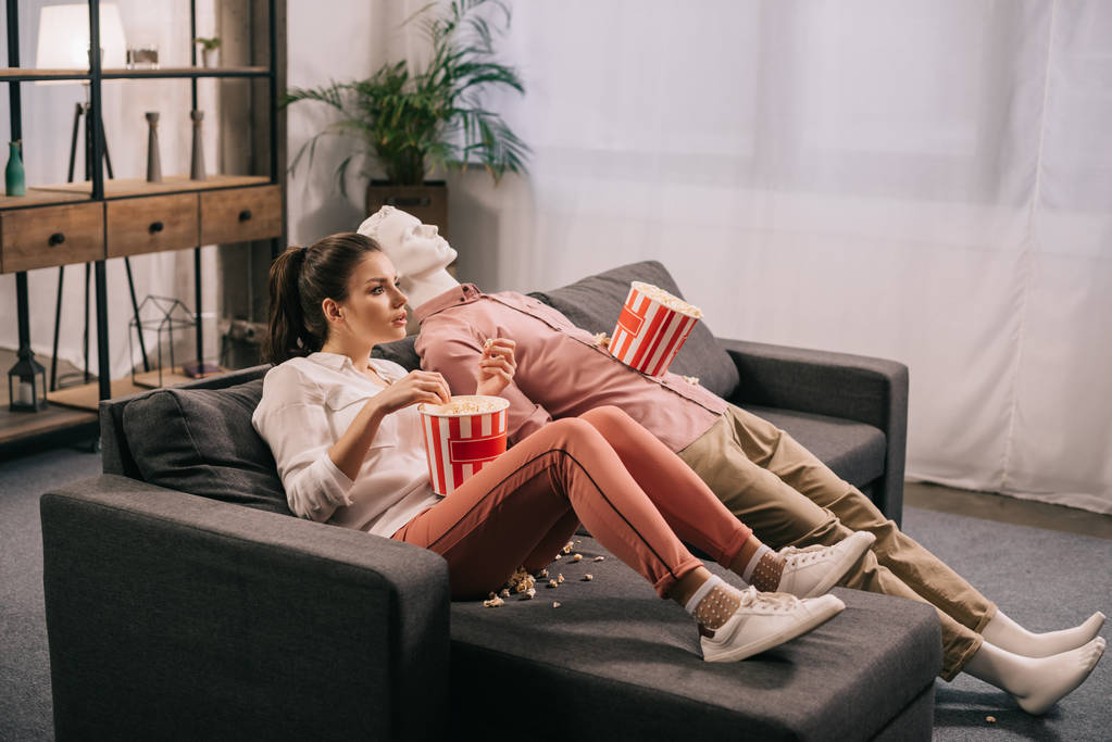 Kobieta jedzenie popcorn podczas oglądania filmu wraz z manekina w domu, koncepcja marzenie doskonałe relacje - Zdjęcie, obraz