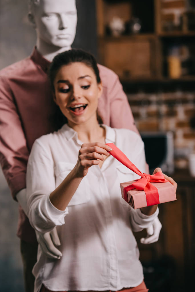excited woman opening gift in hands with manikkin hugging her behind, perfect man dream concept - Photo, Image