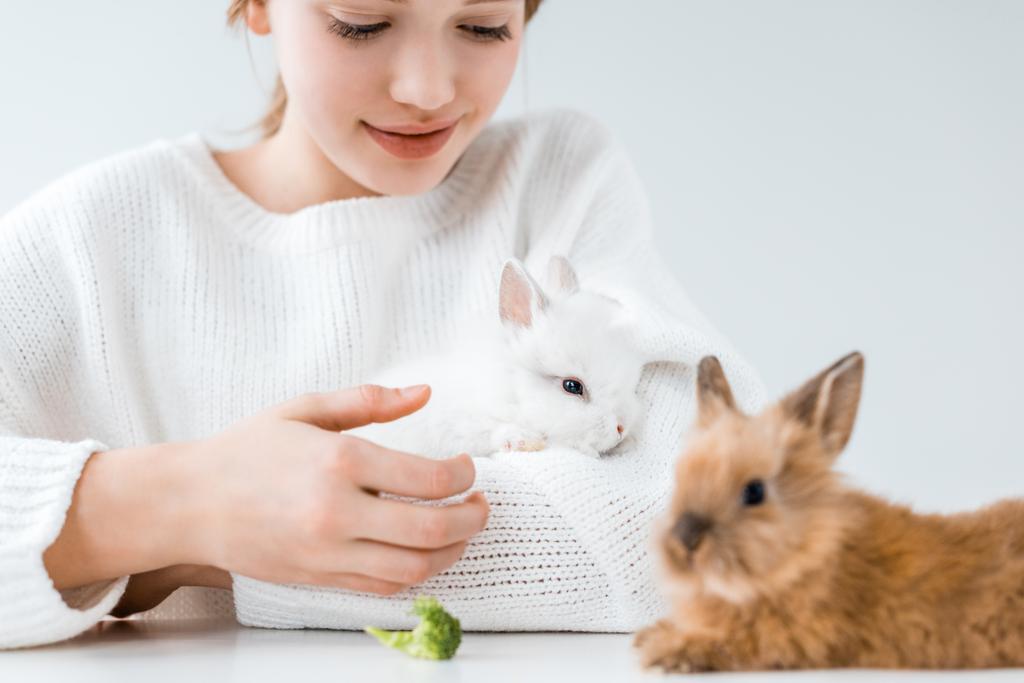 bijgesneden schot van lachende meisje voeding van konijnen met broccoli op wit  - Foto, afbeelding