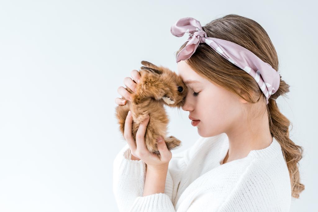 вид сбоку красивой маленькой девочки, держащей пушистого кролика, изолированного на белом
 - Фото, изображение