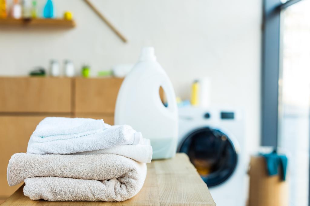 vista de cerca de toallas limpias apiladas y contenedor de plástico con líquido de limpieza en la mesa de madera en casa
  - Foto, Imagen