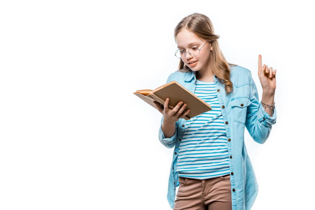 beautiful teenage girl in eyeglasses reading book and pointing up with finger isolated on white - Photo, Image