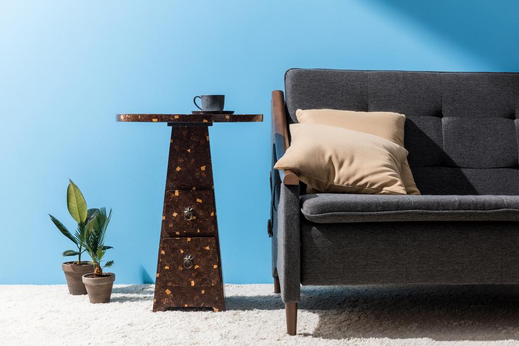 mesa de café com xícara perto do sofá na frente da parede azul
 - Foto, Imagem