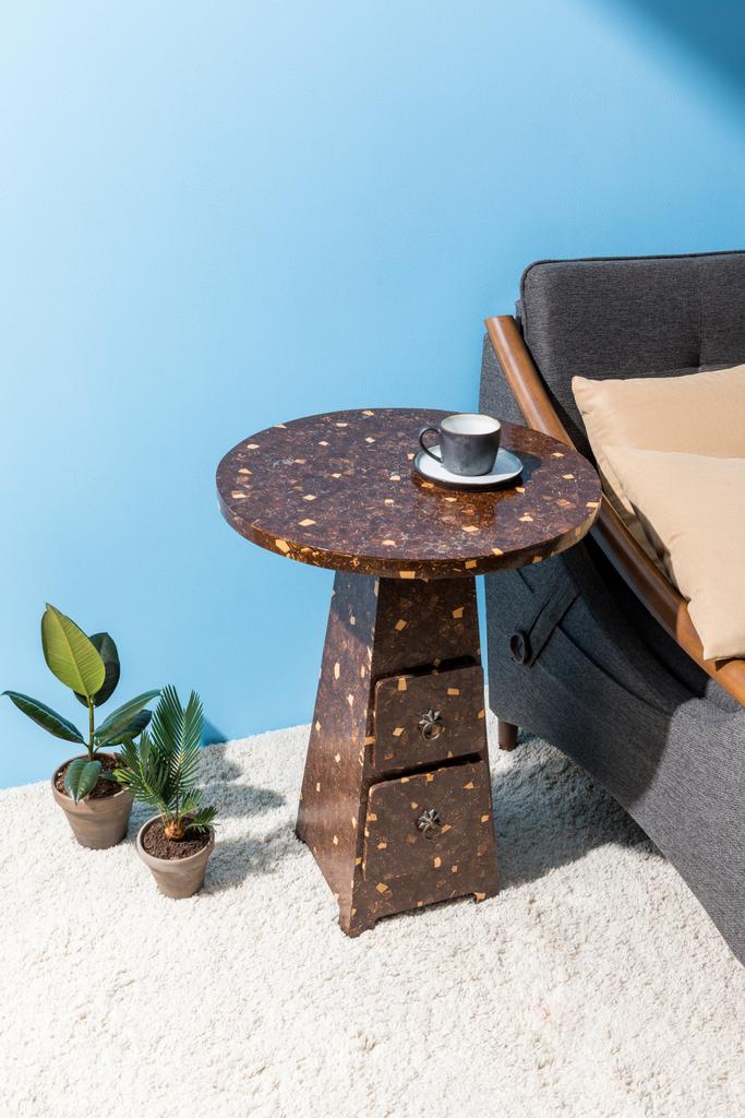 mesa de café com xícara perto de sofá acolhedor na frente da parede azul
 - Foto, Imagem