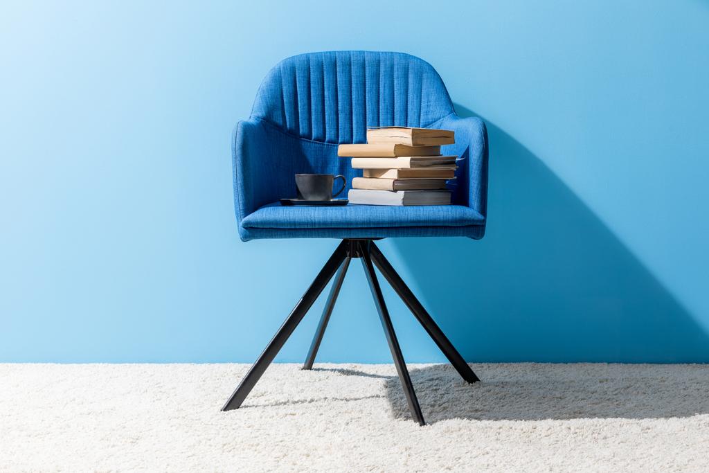 φλιτζάνι καφέ και βιβλία στην καρέκλα μπροστά από το μπλε τοίχο - Φωτογραφία, εικόνα
