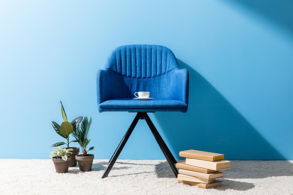 青い壁の前にコーヒーのカップに青い肘掛け椅子快適です - 写真・画像