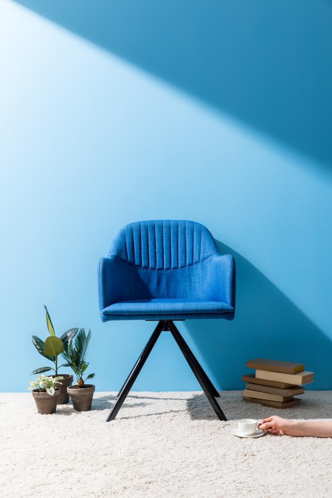 зручне синє крісло з людиною, що тримає чашку кави на підлозі перед синьою стіною
 - Фото, зображення