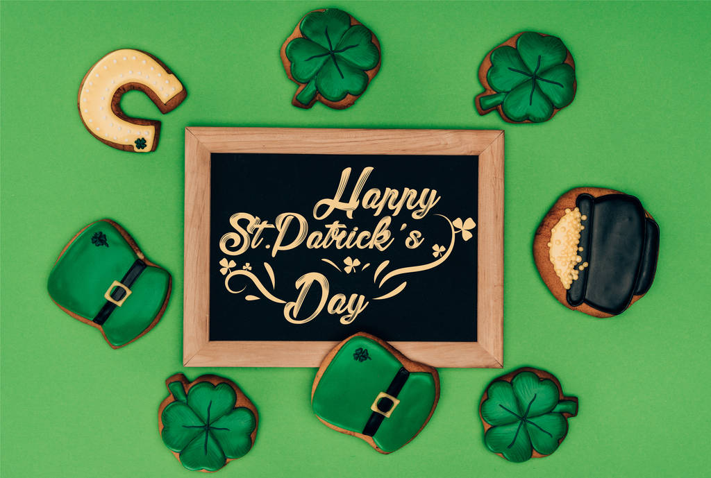 vista superior de galletas festivas y pizarra con letras feliz día de San Patricio aislado en verde
 - Foto, imagen