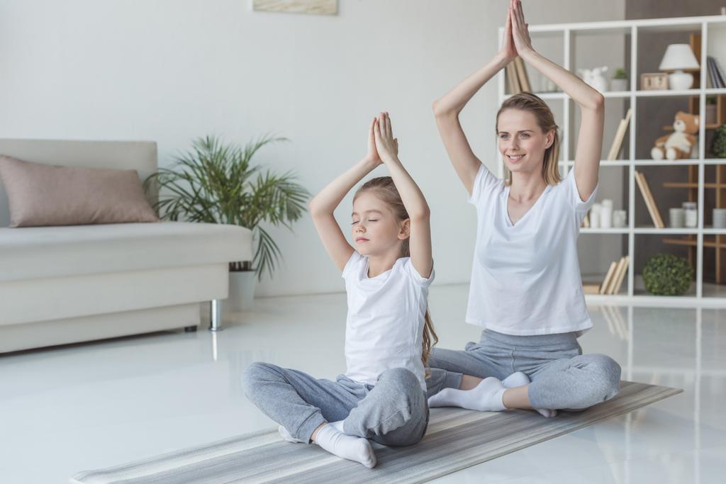 mother and daughter practicing yoga in lotus pose at home - Photo, Image