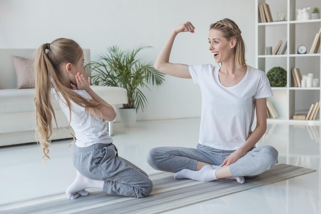 madre mostrando el músculo bíceps a su hija en casa
 - Foto, imagen