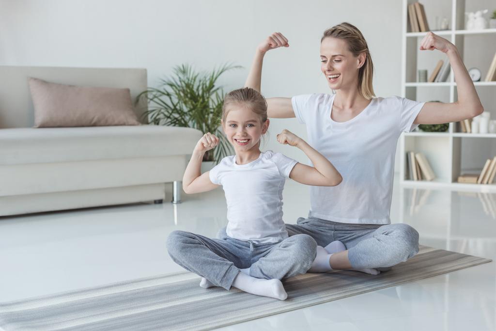 mother and daughter showing muscles on yoga mats - Photo, Image