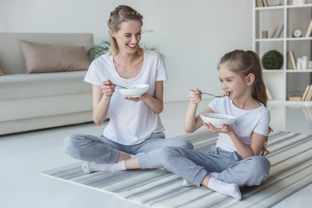 matka i córka jedzenia zbóż posiłek, siedząc na maty do jogi - Zdjęcie, obraz