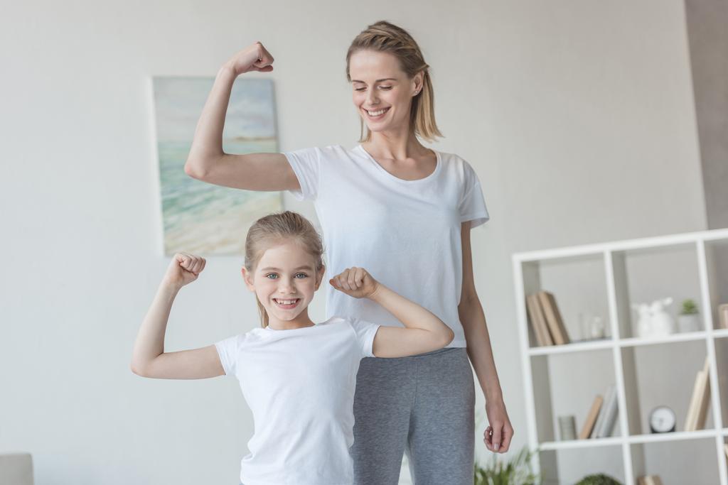 счастливая мать и дочь показывают бицепсы мышц
 - Фото, изображение