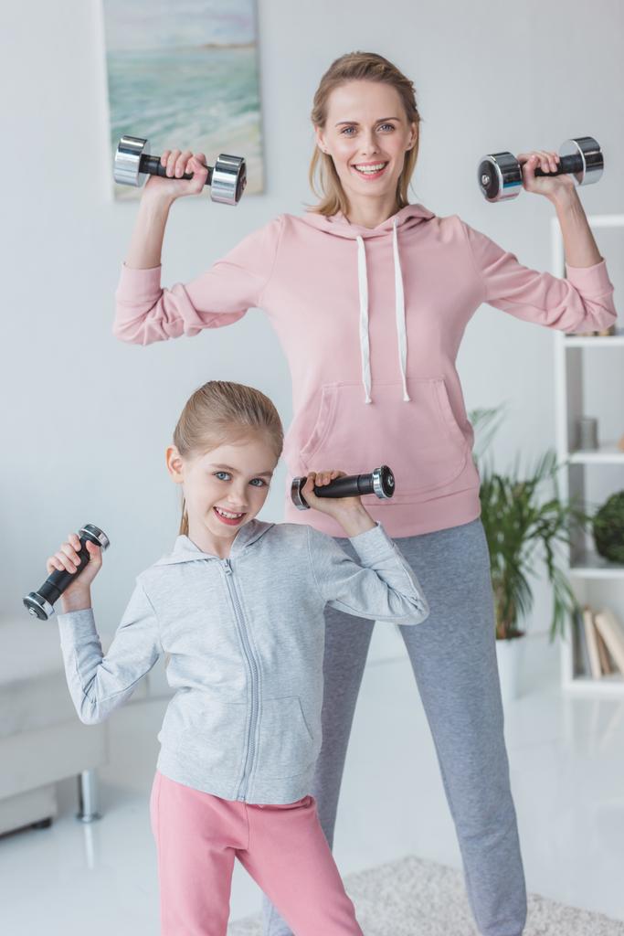 Gesunde Mutter und Tochter trainieren zu Hause mit Kurzhanteln - Foto, Bild