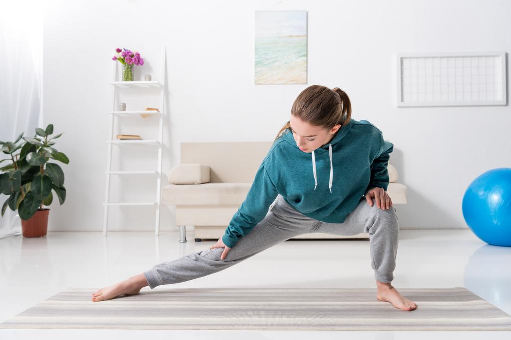girl stretching legs on yoga mat at home - Photo, Image
