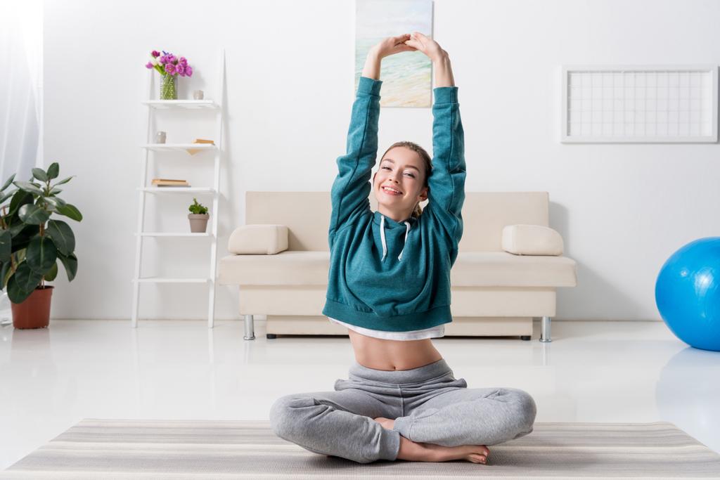 chica sonriente sentada en posición de loto y haciendo yoga en casa
 - Foto, Imagen