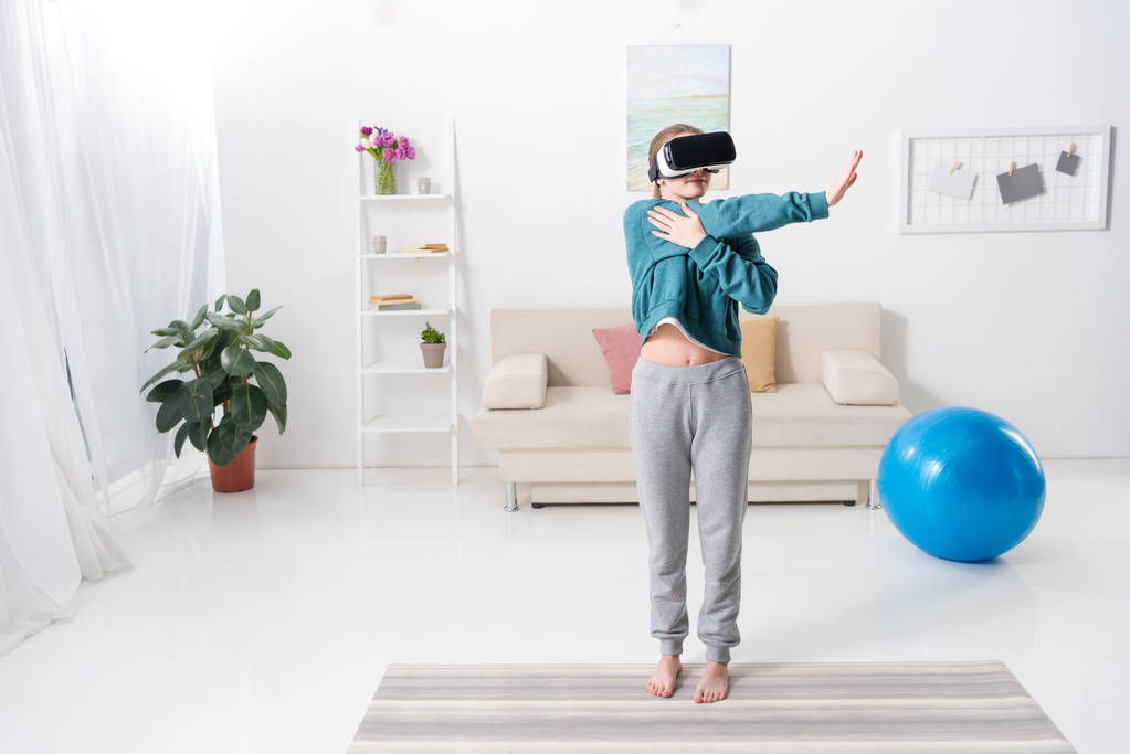 Dziewczyna, rozciągając ręce z zestaw wirtualnej rzeczywistości na matę do jogi w domu - Zdjęcie, obraz
