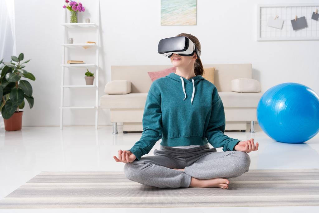menina sentada na posição de lótus com fone de ouvido realidade virtual em casa
 - Foto, Imagem