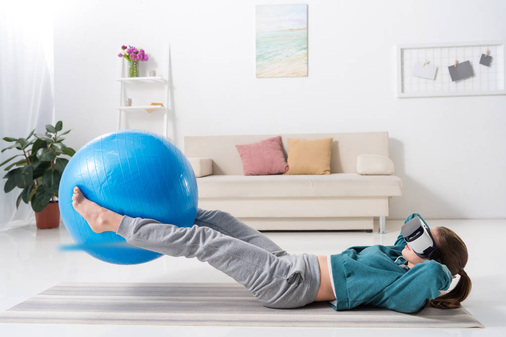 Mädchen trainieren mit Fitnessball und Virtual-Reality-Headset zu Hause - Foto, Bild